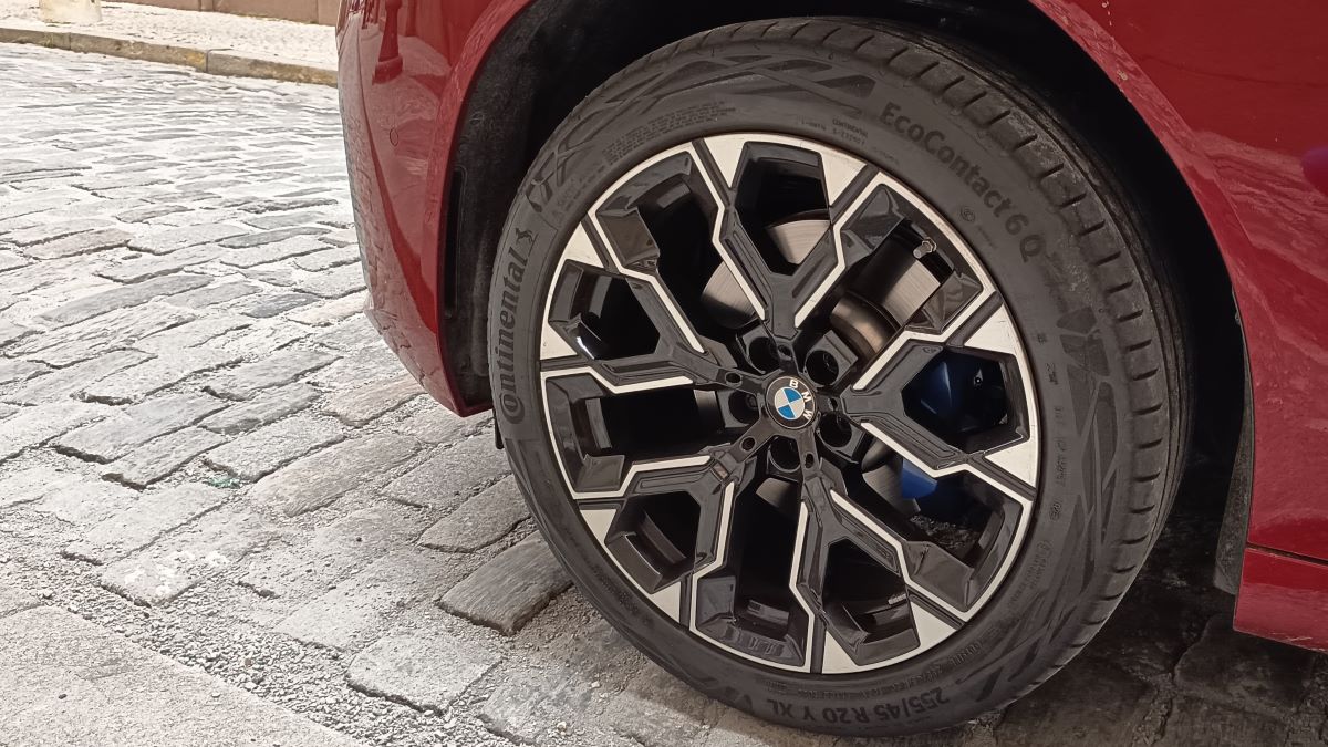 Roda de um carro BMW com design elegante, mostrando a roda e o pneu Continental, estacionada em uma rua de paralelepípedo.