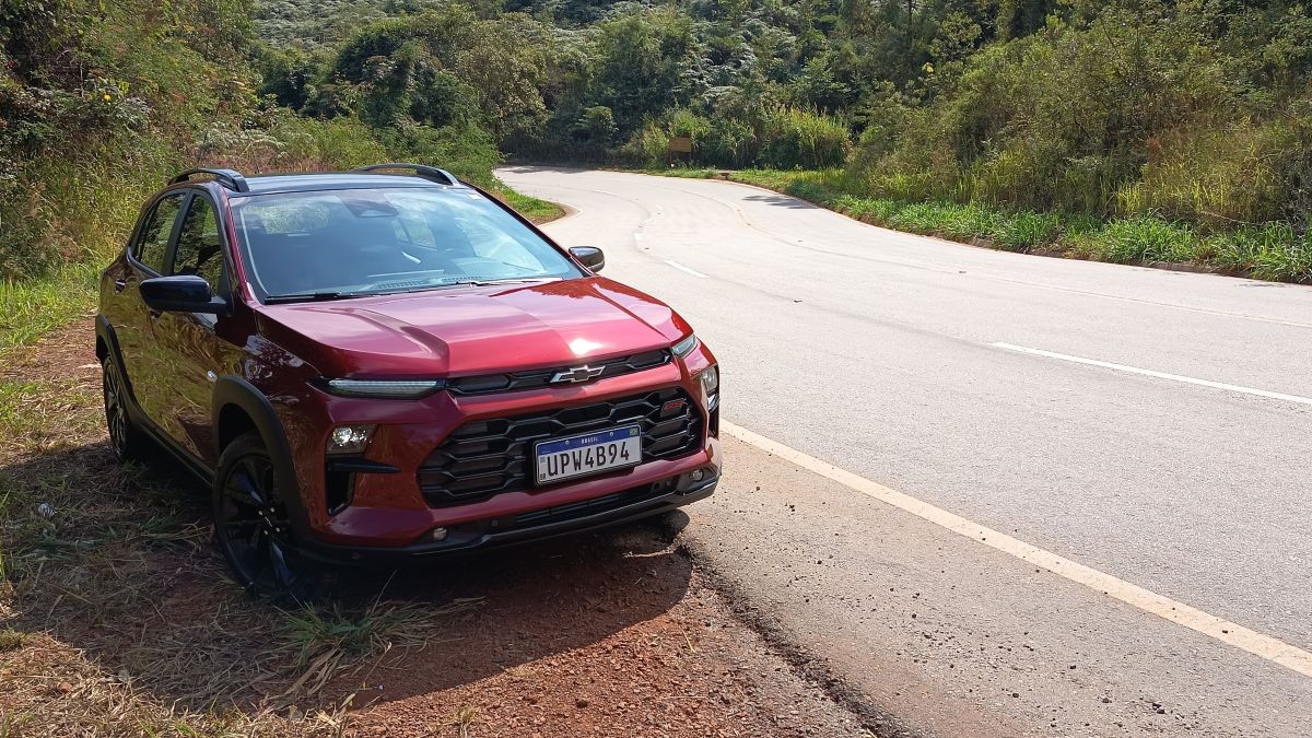 Um carro vermelho estacionado ao lado de uma estrada sinuosa, cercado por vegetação.