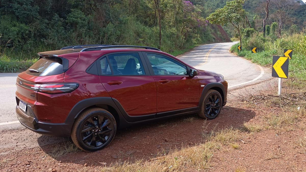 Um carro SUV vermelho estacionado à beira de uma estrada sinuosa, cercada por vegetação.
