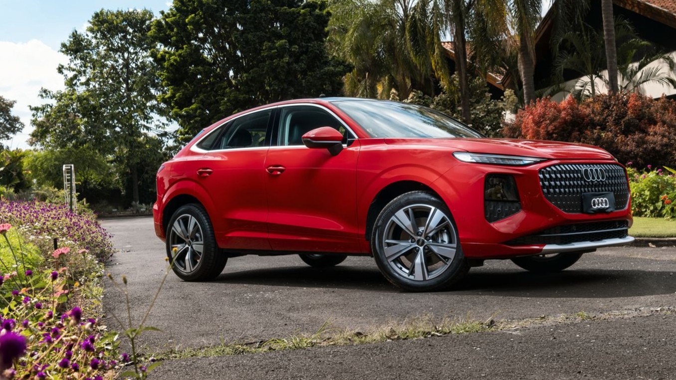 Carro vermelho da marca Audi em uma estrada cercada por flores e árvores.