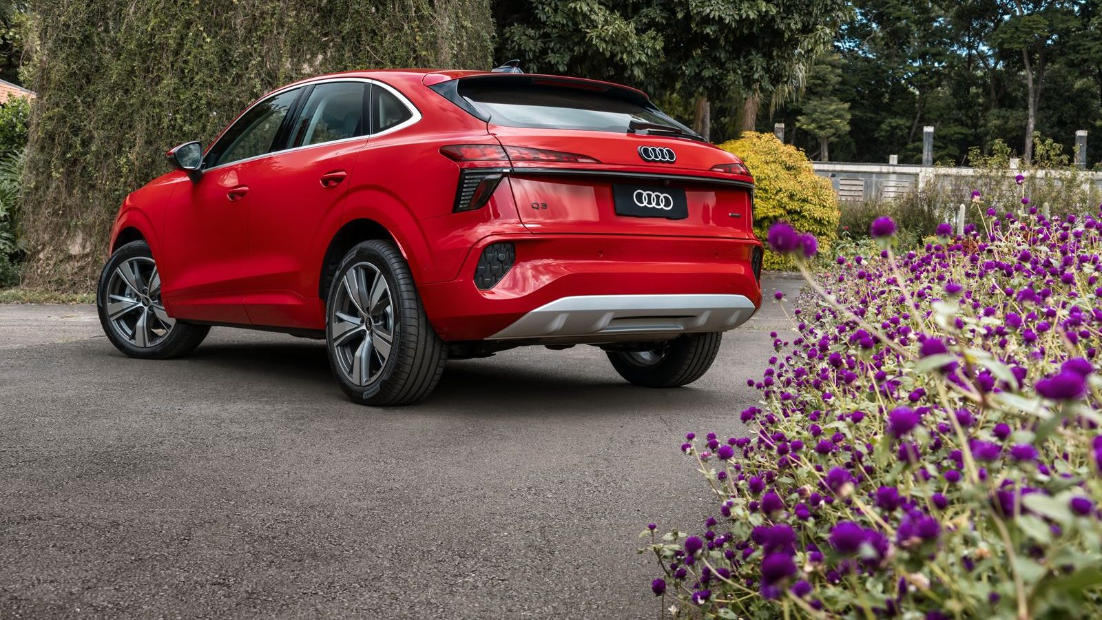 SUV Audi Q3 vermelho estacionado em uma rua com flores roxas ao redor.