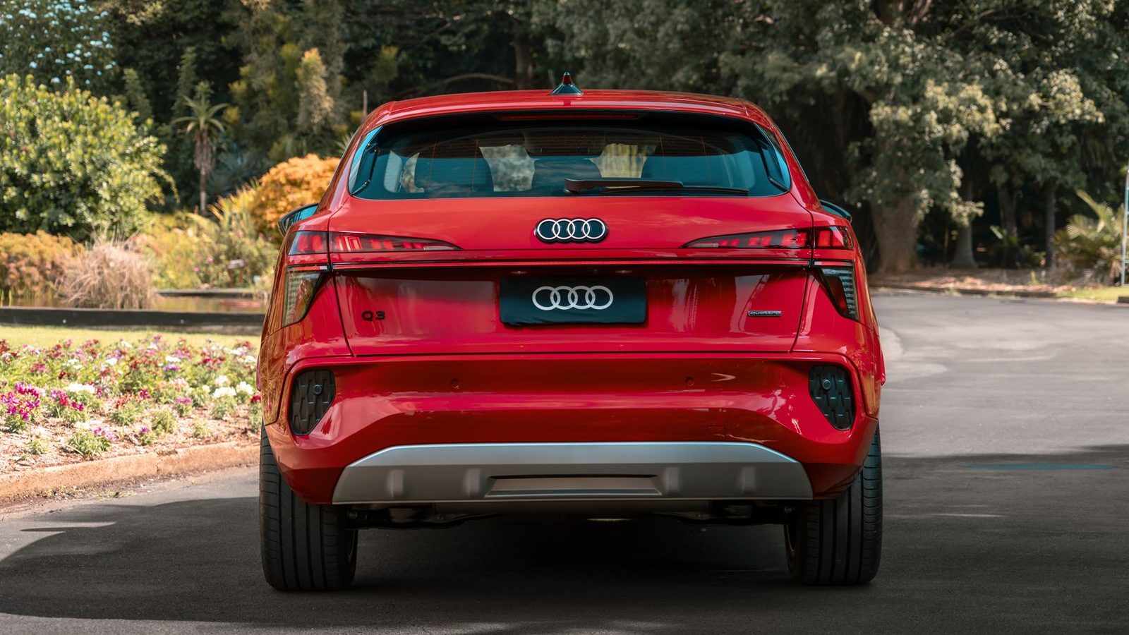Traseira de um carro Audi Q3 vermelho estacionado em uma estrada, com vegetação ao fundo.