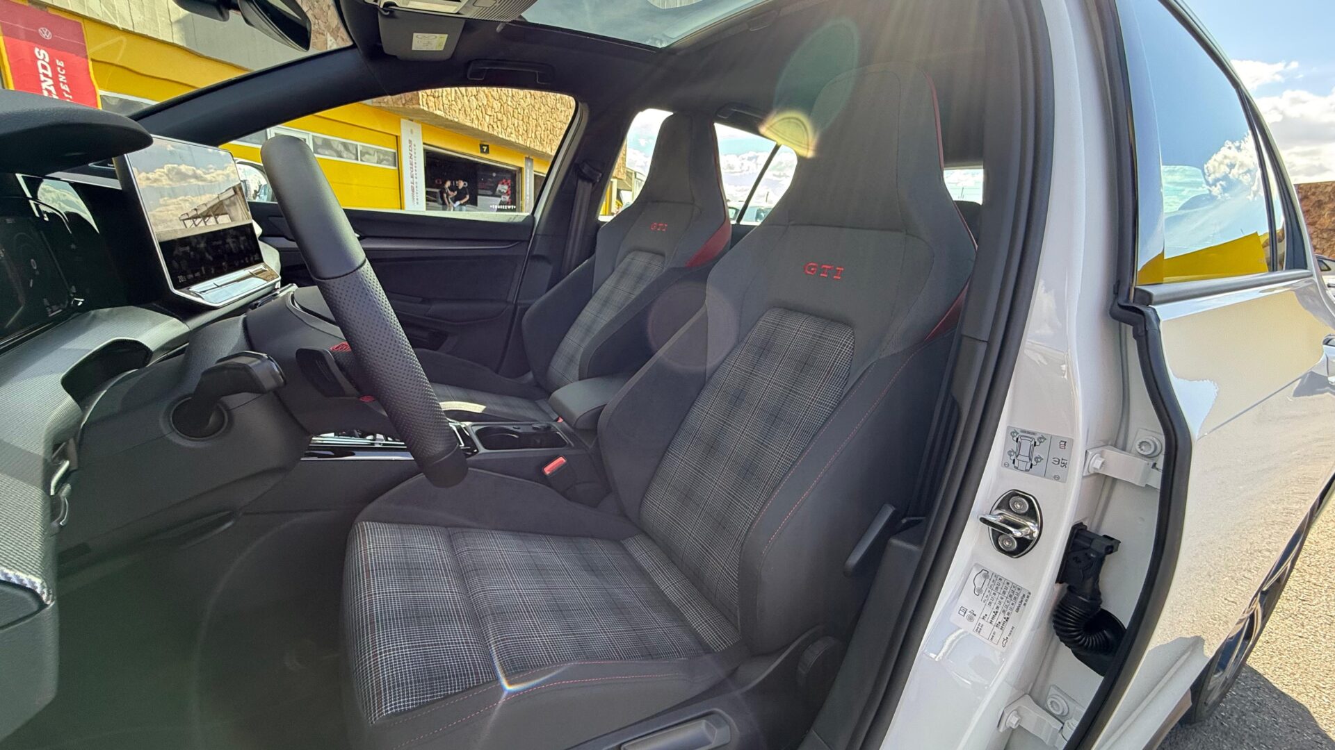 Interior de carro esportivo com bancos em tecido xadrez e detalhes em vermelho, volante bem projetado e tela multimídia.