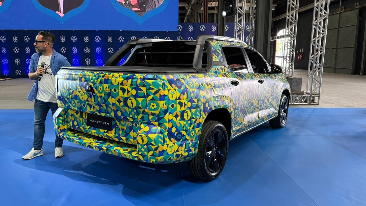 Um homem com microfone apresenta uma picape Volkswagen decorada com um padrão colorido em uma exposição.