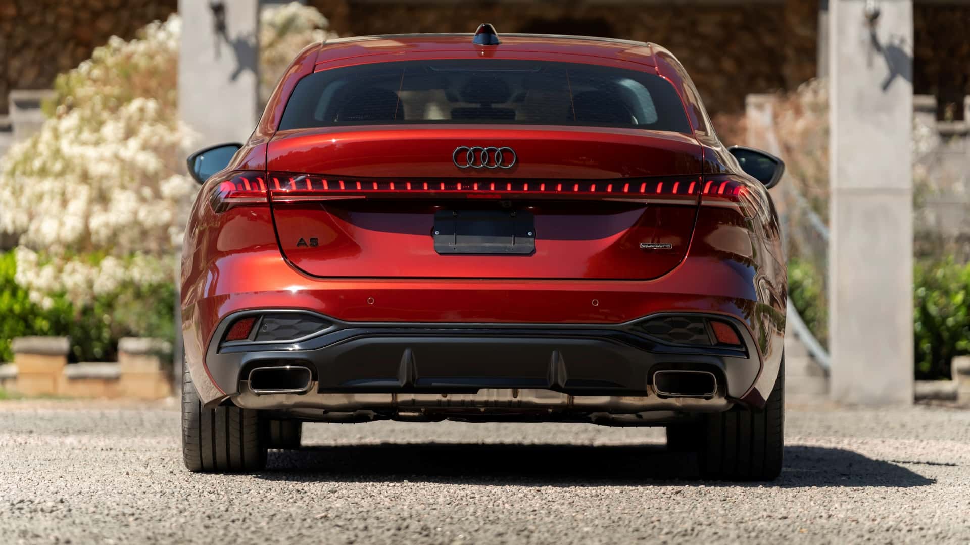Vista traseira de um carro Audi A5 vermelho em um ambiente ao ar livre, com flores e vegetação ao fundo.