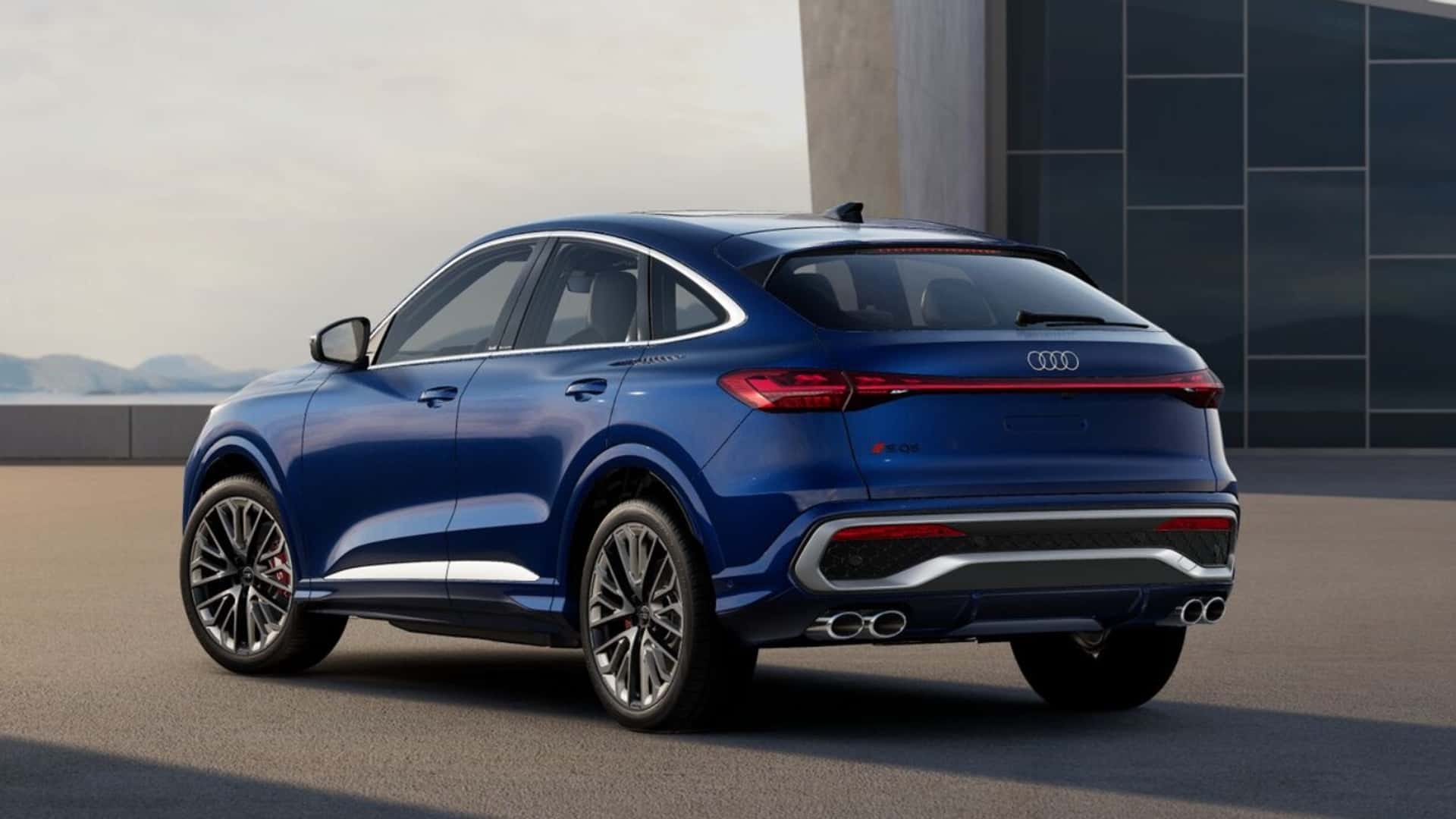 Vista traseira de um carro SUV azul da Audi, exibindo design moderno e rodas esportivas, estacionado em uma superfície externa com um fundo minimalista.