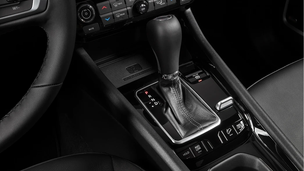 Imagem do console central de um carro, destacando a alavanca de câmbio automática com acabamento em couro e os botões de controle.