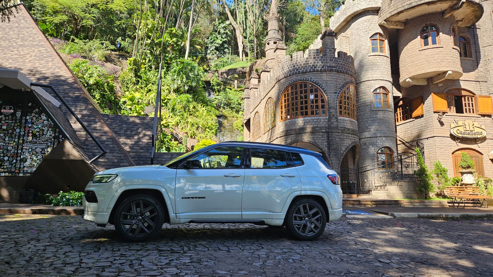 Um carro SUV branco estacionado em frente a um edifício de estilo medieval, cercado por vegetação exuberante.