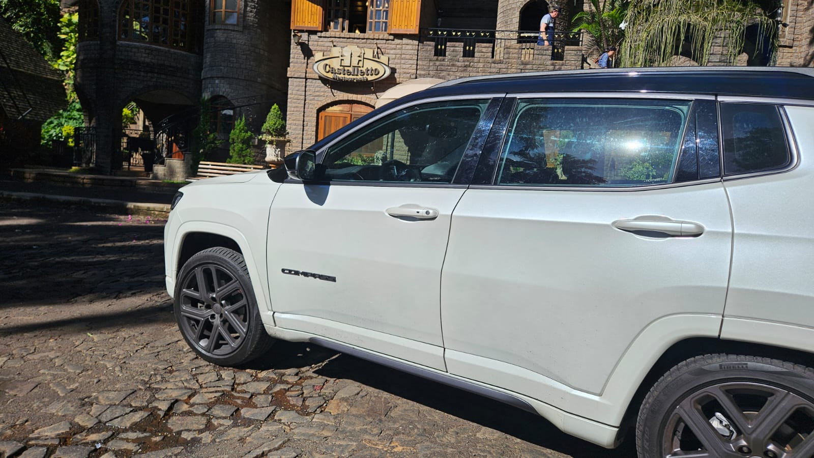 Automóvel SUV branco estacionado em frente a um edifício de pedra com janelas grandes e varanda.