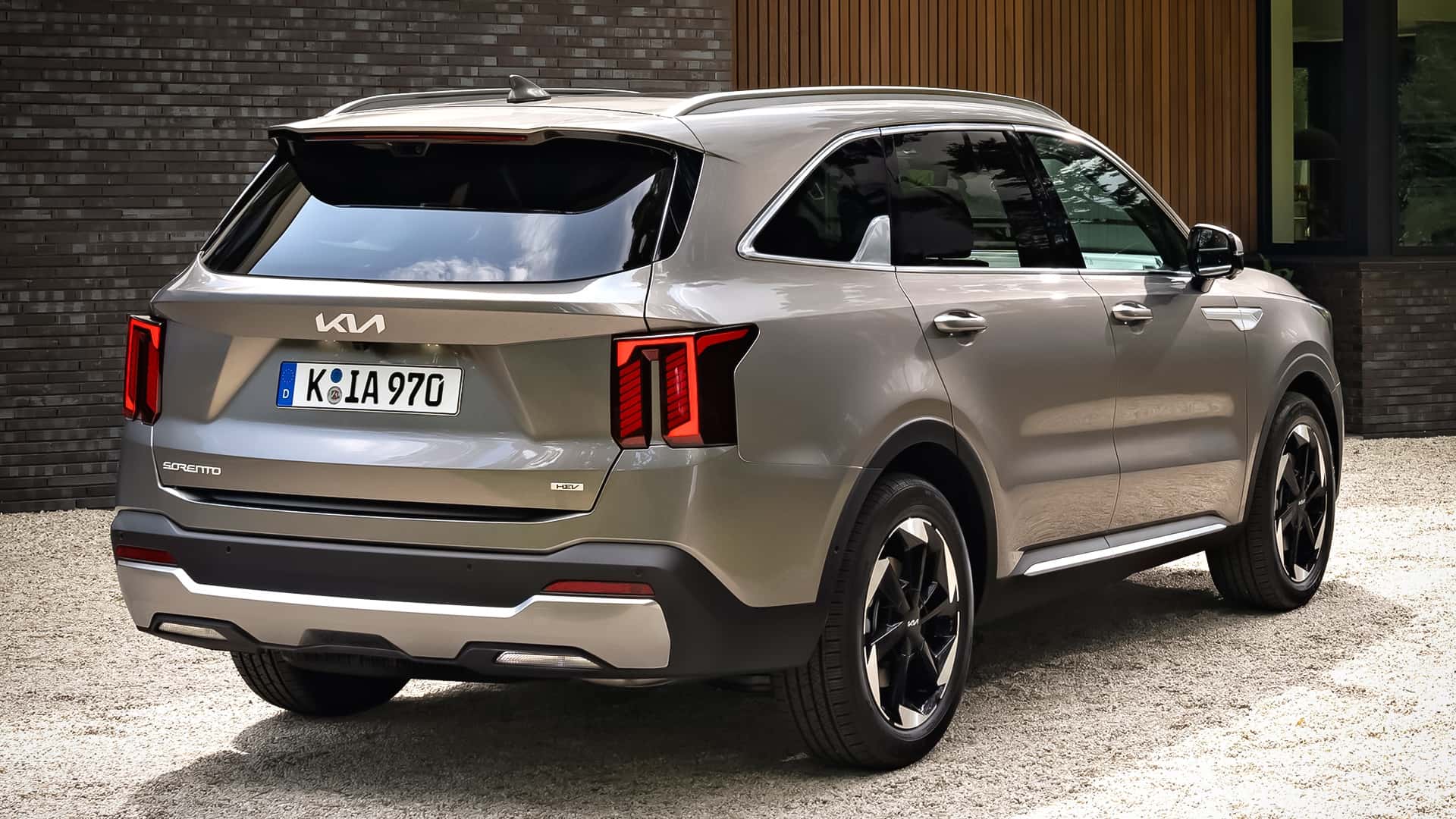 A SUV Kia Sorento na cor prata, vista de trás, estacionada em uma superfície de cascalho. A imagem destaca as lanternas traseiras e a placa do veículo.