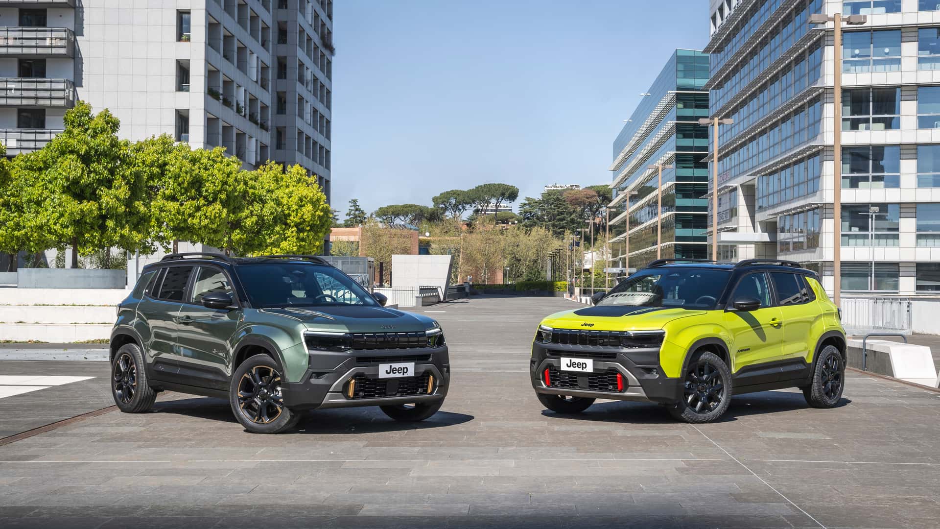 Dois SUVs da Jeep em uma área urbana, um verde e outro amarelo, com edifícios modernos ao fundo.