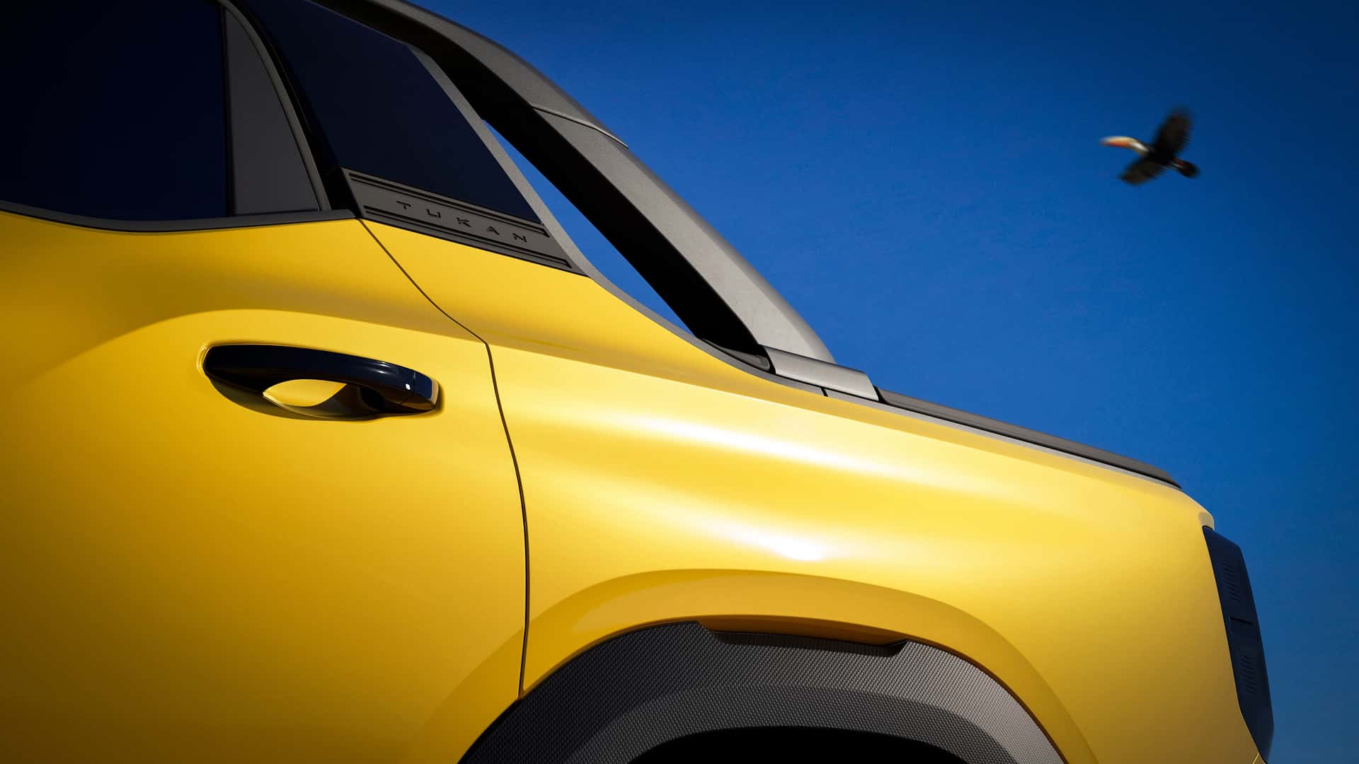 Detalhe lateral de um carro amarelo com um céu azul ao fundo, destacando a maçaneta e o emblema 'Tukan'.