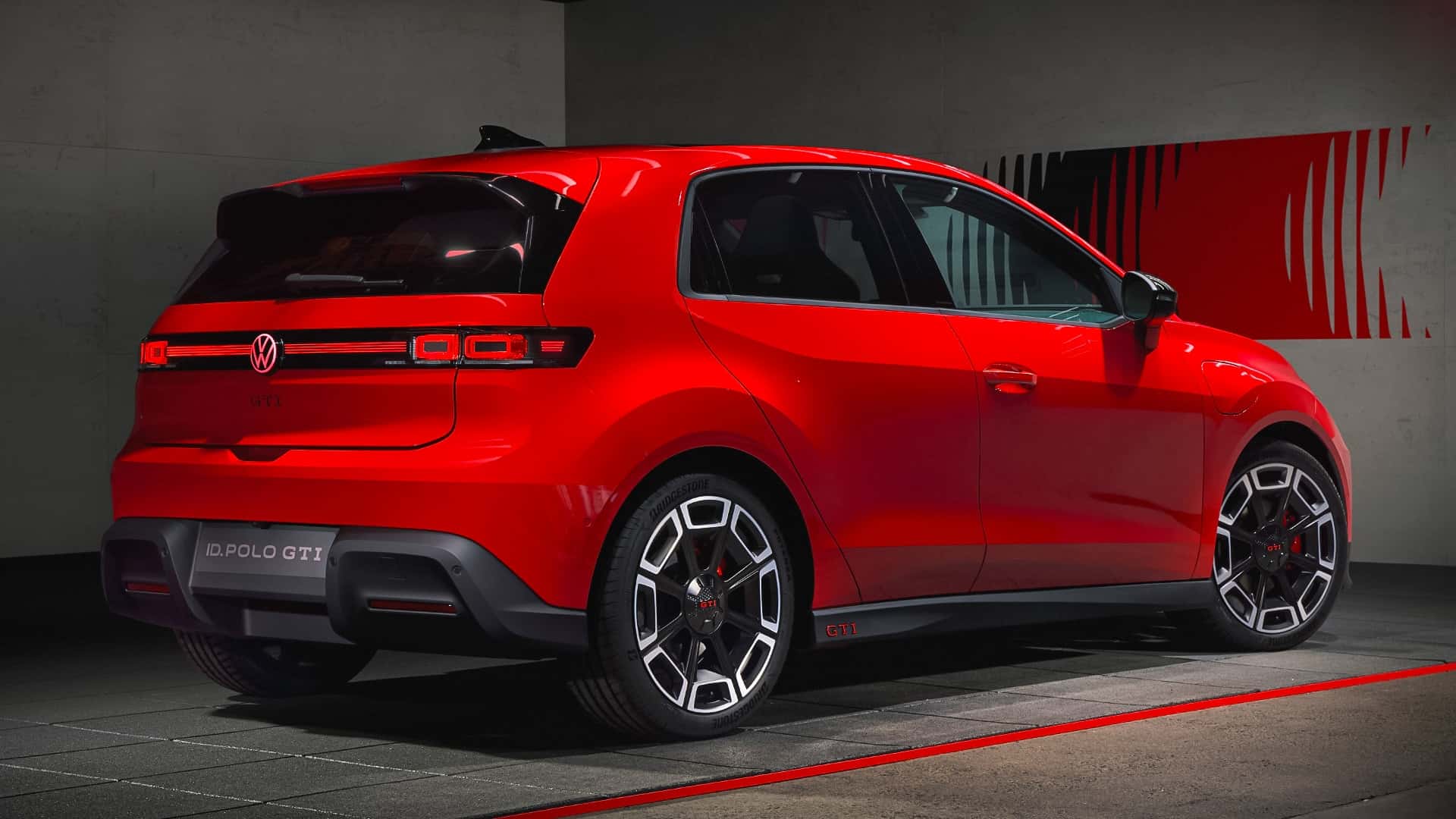 Volkswagen ID. Polo GTI vermelho com detalhes esportivos, visto de trás em um ambiente moderno e escuro.