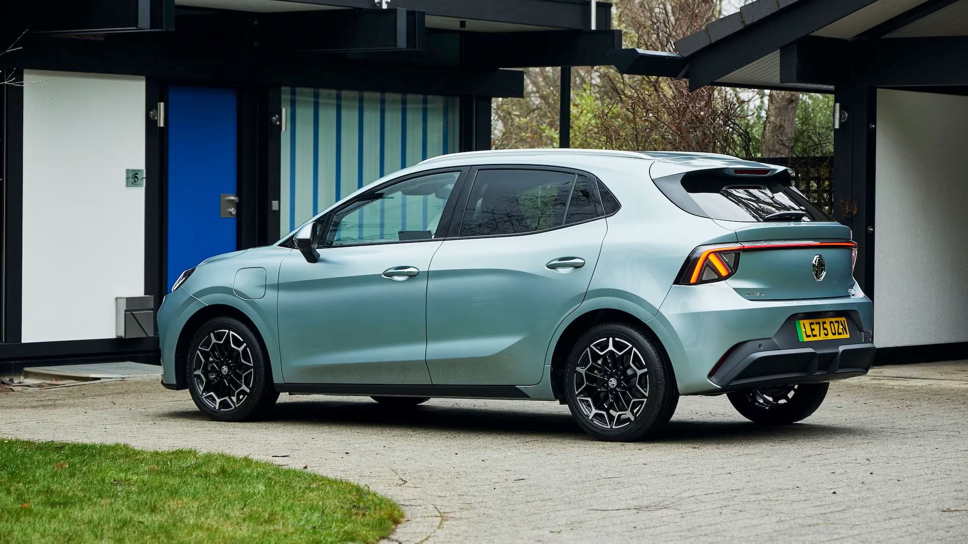 Um carro hatchback da Renault estacionado em frente a uma casa moderna, com uma fachada clara e detalhes em azul.