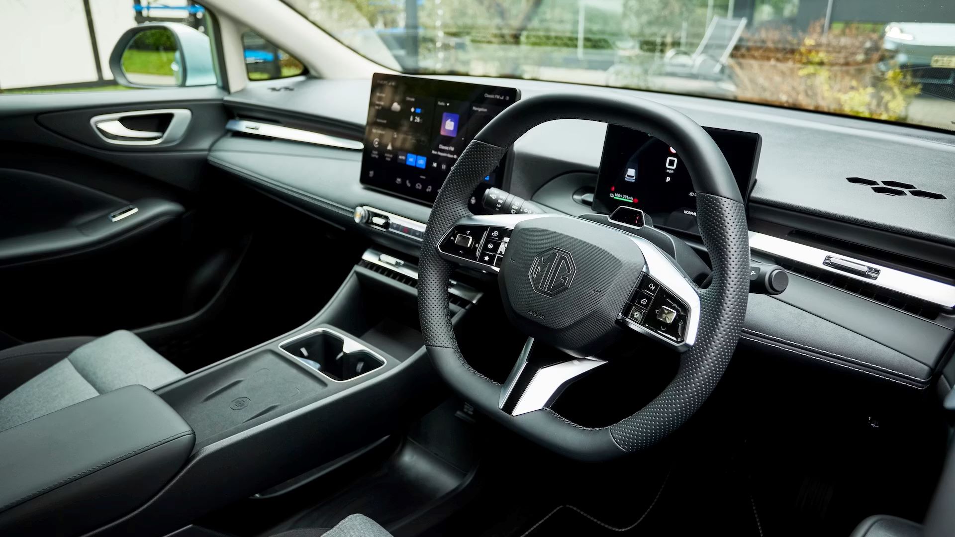 Interior de um carro mostrando o volante, painel touchscreen e console central em tons de preto e cinza.
