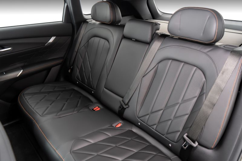 Interior do banco traseiro de um carro, com estofamento em couro preto e detalhes em costura laranja.