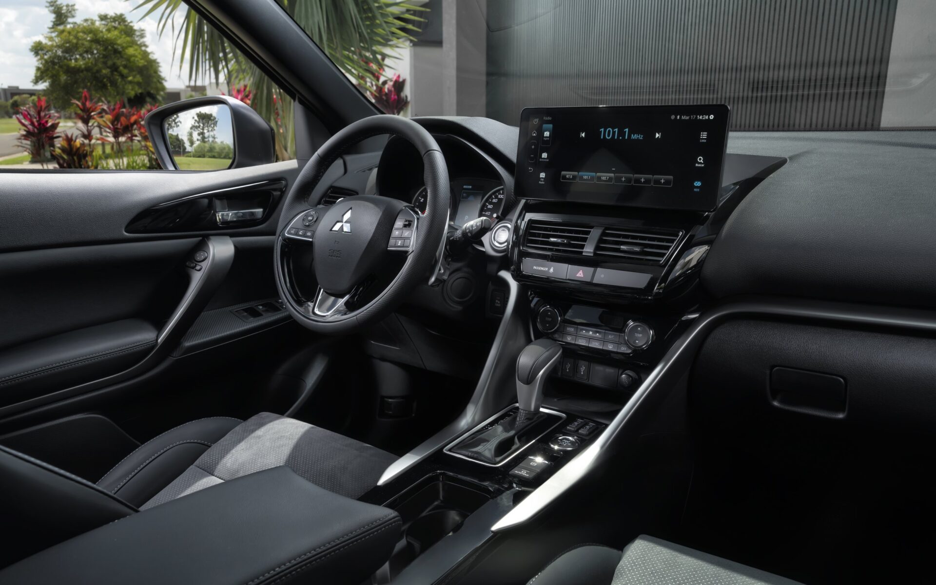 Interior view of a modern car dashboard featuring a steering wheel, touchscreen display, and gear shift surrounded by black and gray upholstery.
