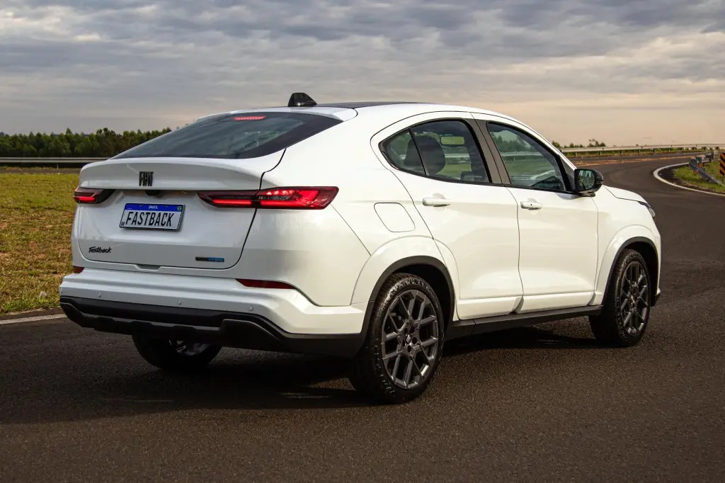 A white compact SUV parked on a winding road, showcasing a sleek design and sporty wheels, with the 'FASTBACK' badge visible on the rear.