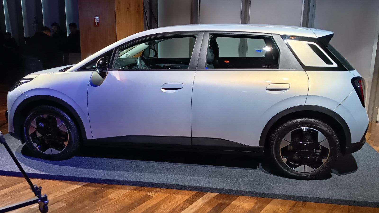 Um carro elétrico de cor prata exibido em um evento, com design moderno e rodas esportivas pretas.