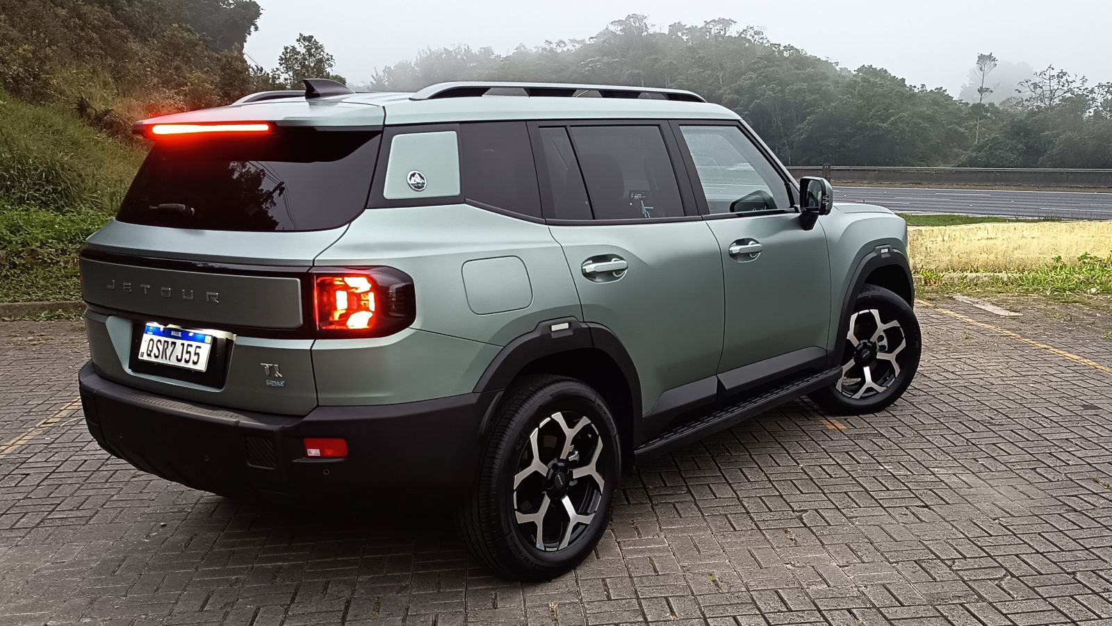 SUV Jetour em uma área de estacionamento, com um fundo de vegetação e neblina.