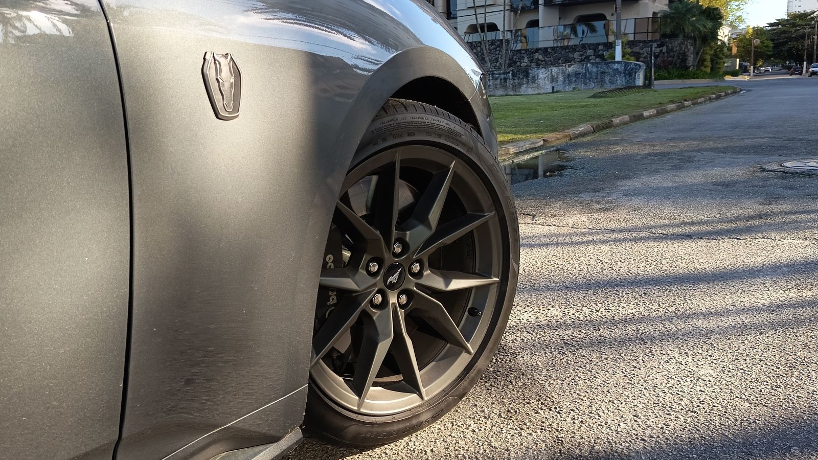 Detalhe da roda de um carro esportivo cinza, mostrando o logotipo e o design do aro.