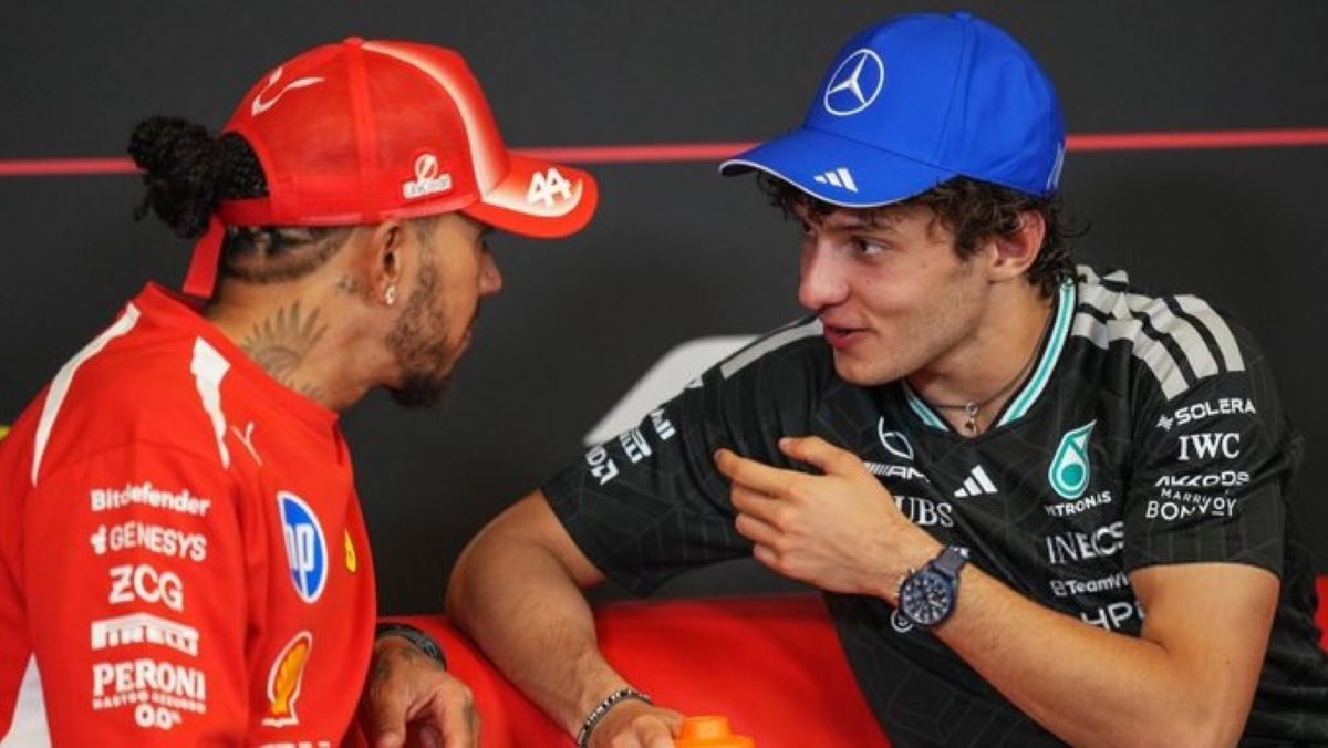 Dois pilotos de Fórmula 1 conversando, um vestindo uniforme da Ferrari e um com uniforme da Mercedes.