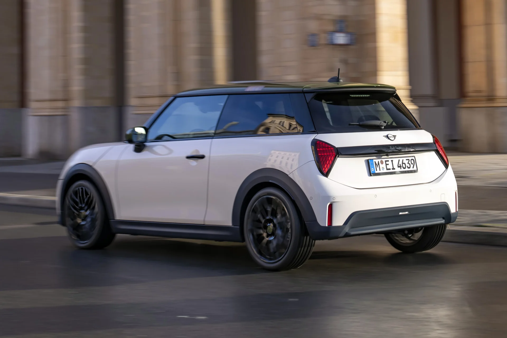 A white compact car with a black roof and sporty design, driving on a city street.
