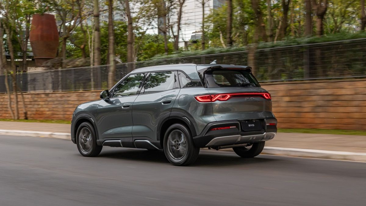 SUV cinza se movendo em uma rua, com árvores ao fundo e um muro de pedra.