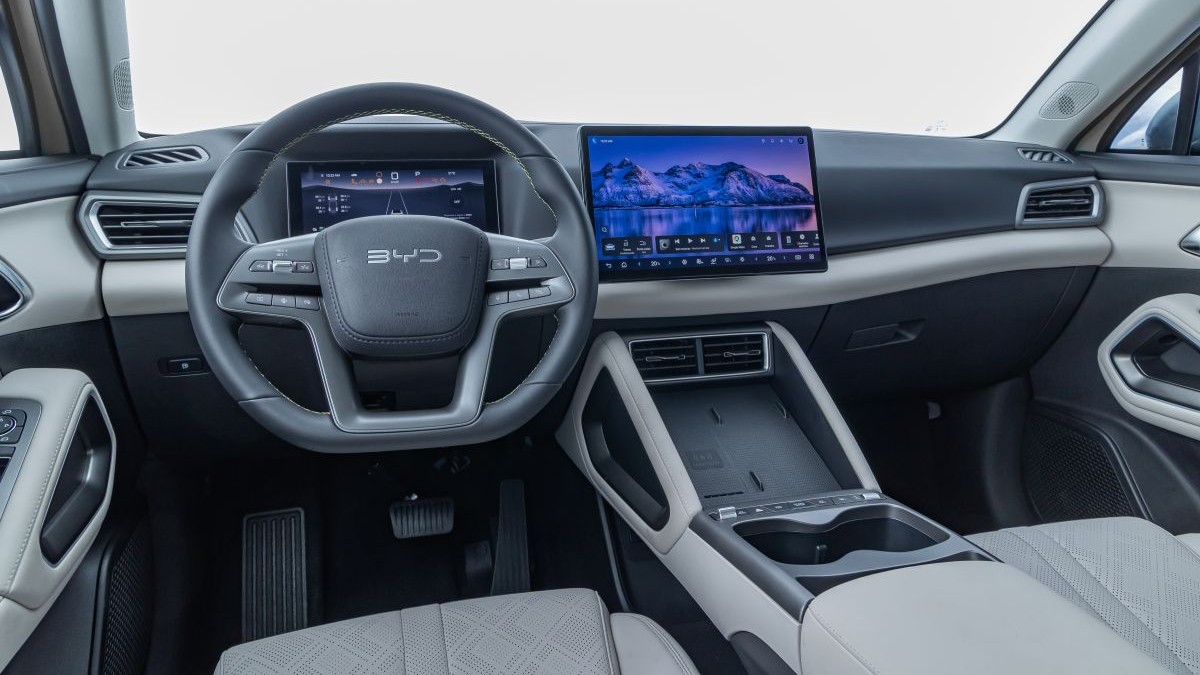 Interior de um carro elétrico com volante moderno, painel digital e grande tela central.