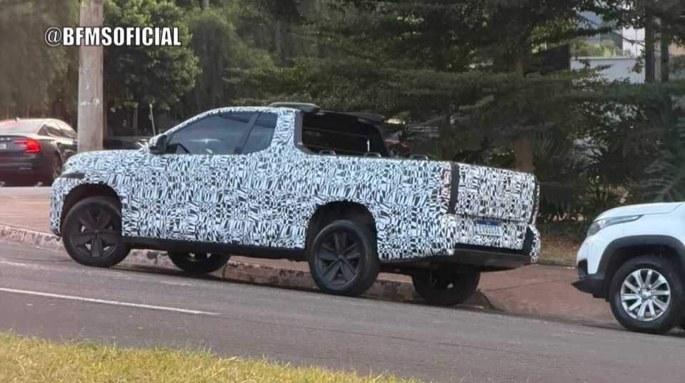 A camouflaged pickup truck parked on the side of the road, surrounded by trees and another vehicle nearby.