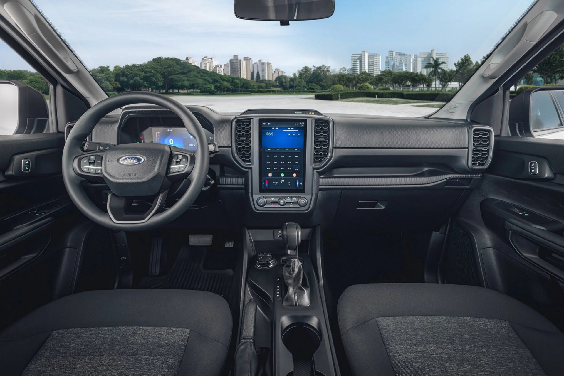 Interior view of a Ford vehicle showcasing the steering wheel, dashboard with digital display, and gear shift, set against an urban backdrop.
