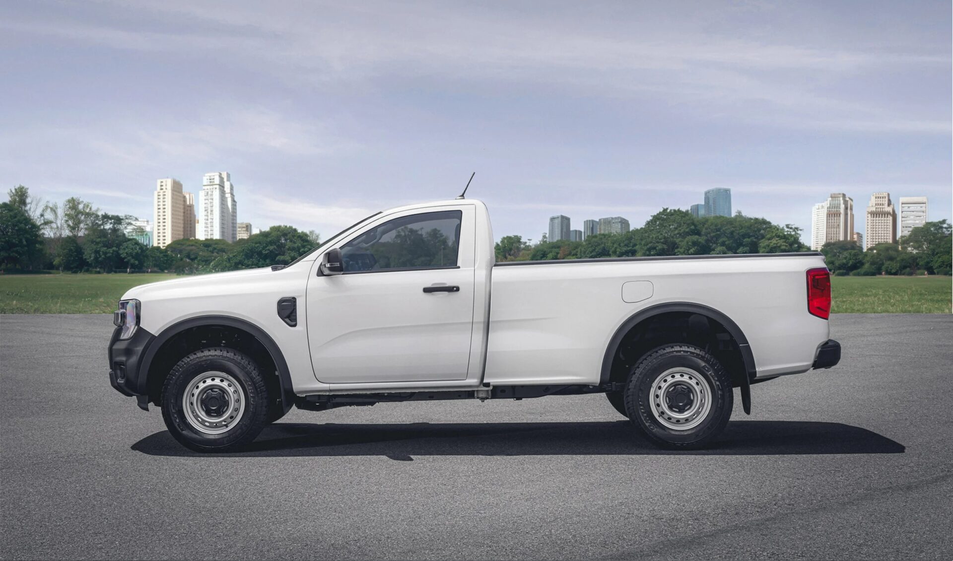 White pickup truck parked on asphalt with a city skyline in the background.