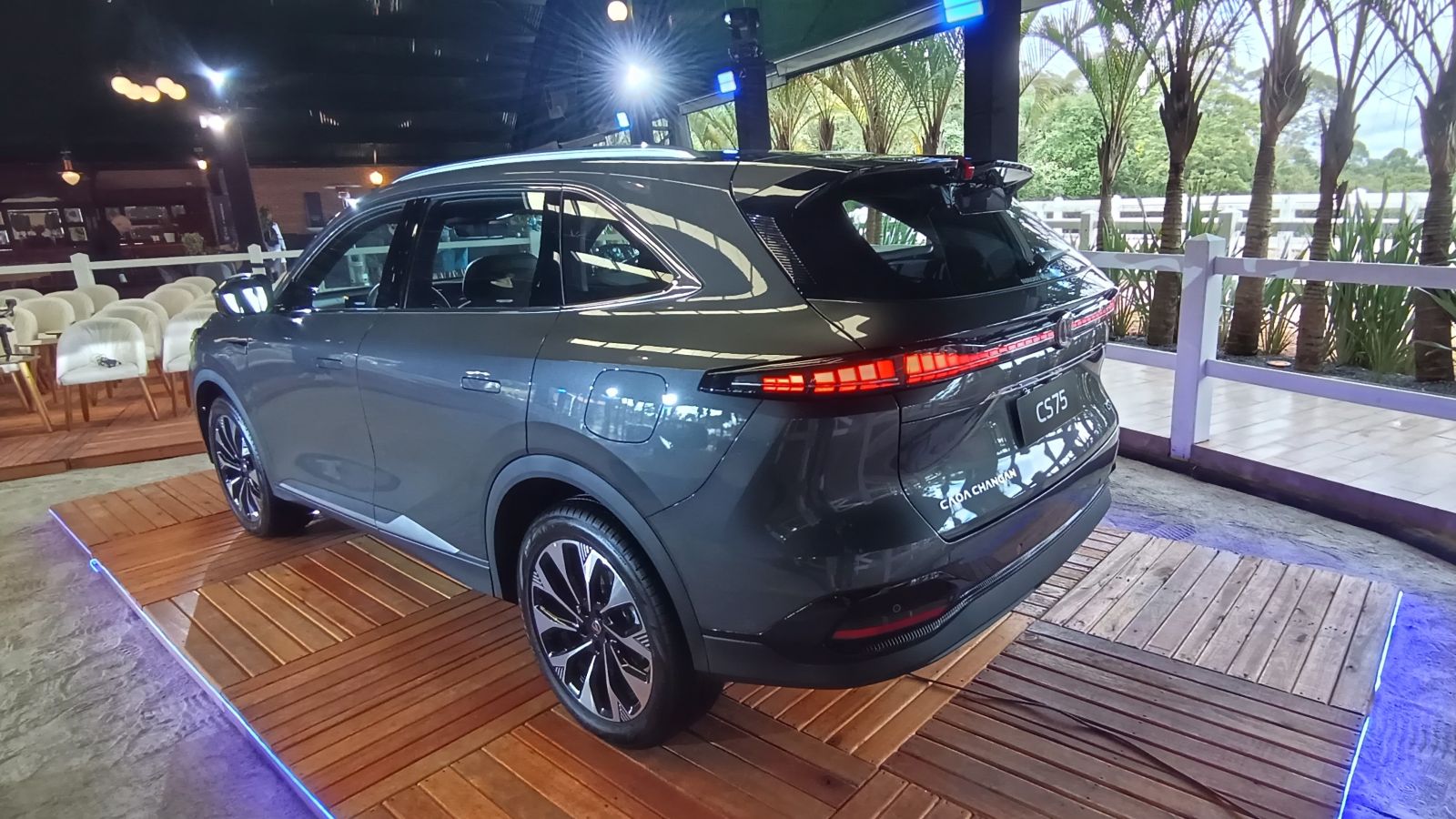 SUV cinza exposto em um evento, com design moderno e elegante, exibindo sua traseira e rodas, montado sobre uma plataforma de madeira iluminada.