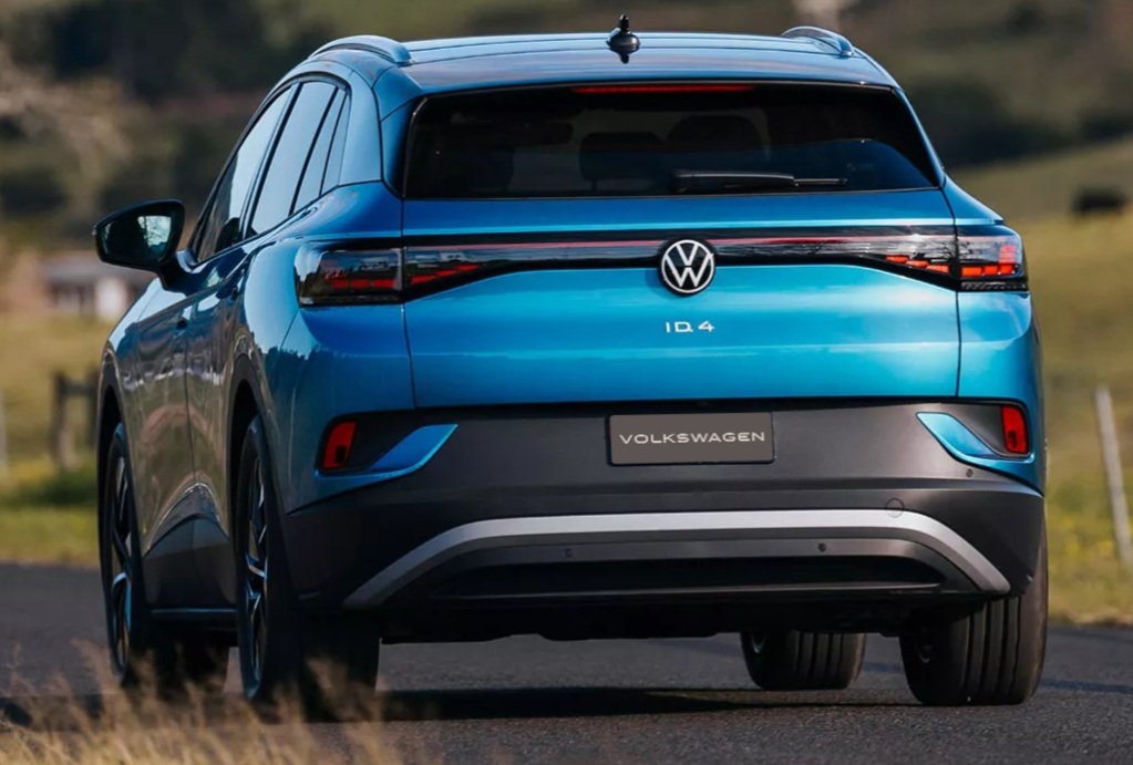 Rear view of a blue Volkswagen ID.4 electric SUV on a road surrounded by green fields.