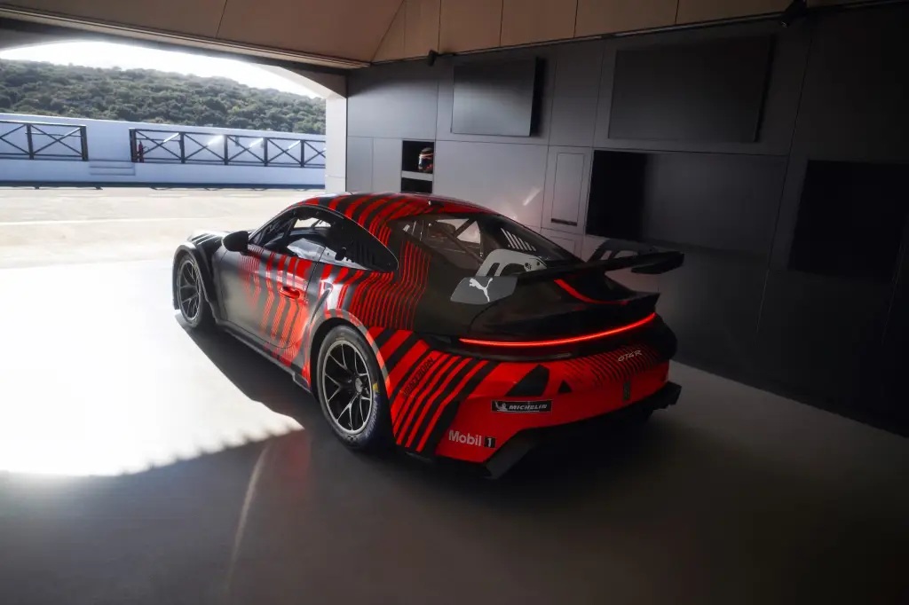 A rear view of a sleek race car with a striking red and black design, parked in a modern garage with a scenic background.