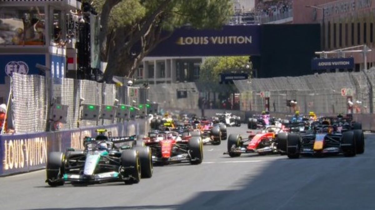 Carros de Fórmula 1 competindo em uma corrida, com o logo da Louis Vuitton ao fundo e espectadores assistindo.