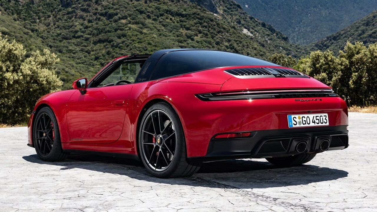 Rear view of a red sports car parked on a stone surface with mountains in the background.
