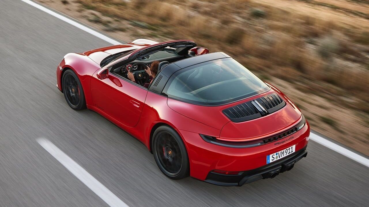 A red convertible sports car driving on a winding road, with the driver visible in the cockpit.