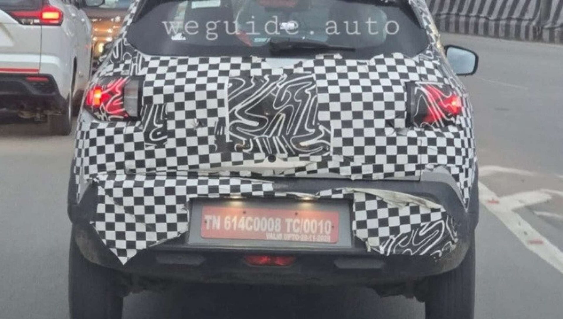 A partially covered car with a checkered camouflage pattern on its rear, showing red tail lights and a license plate.