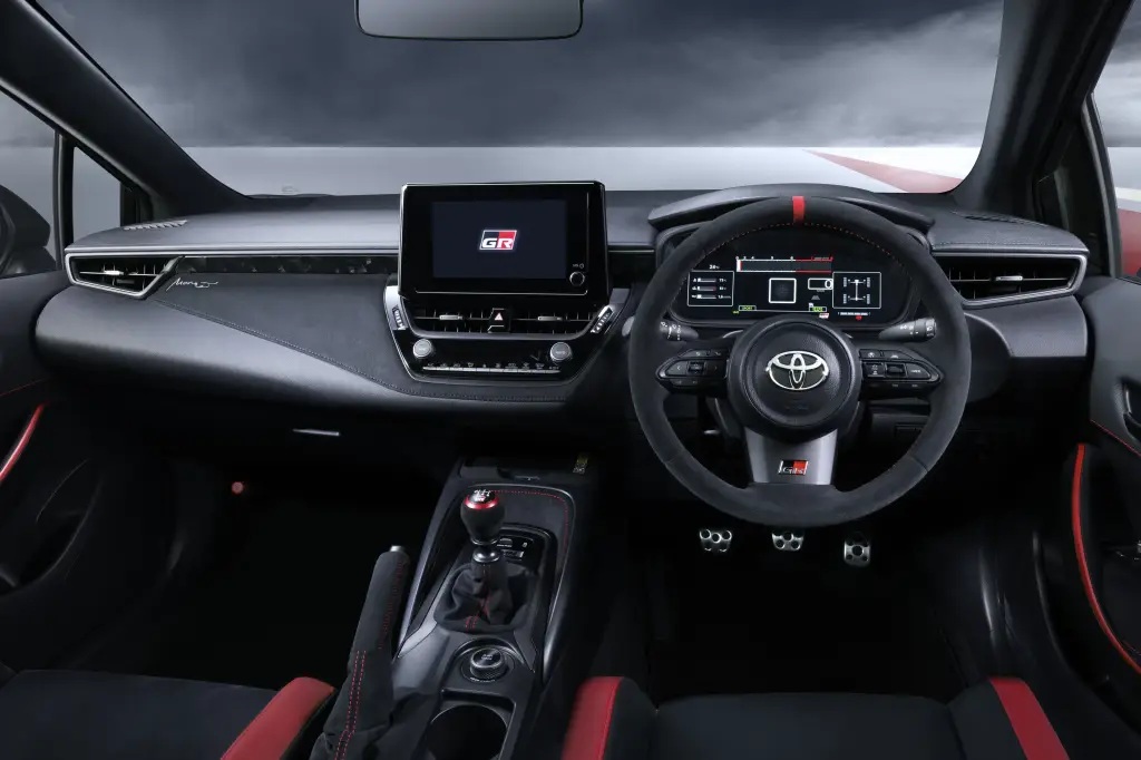 Interior view of a Toyota car showcasing a modern dashboard, touch screen display, steering wheel with controls, and sporty accents in black and red.
