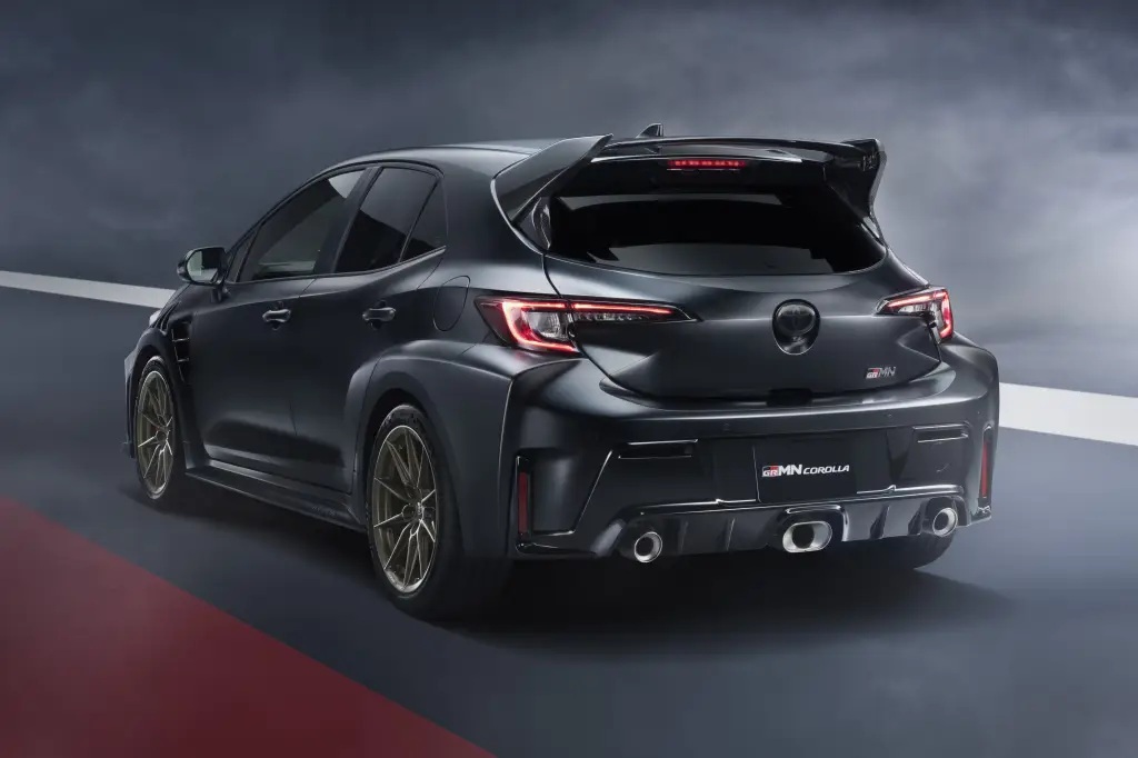 Rear view of a black Toyota GR Corolla showcasing its sporty design, distinctive tail lights, and dual exhausts on a gradient background.