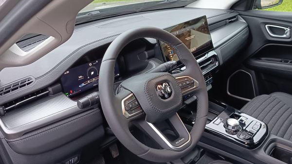Interior de um carro mostrando o volante, painel digital e console central.