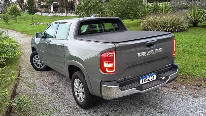 Uma caminhonete RAM prata estacionada em uma área verde, com a traseira visível e capô coberto.