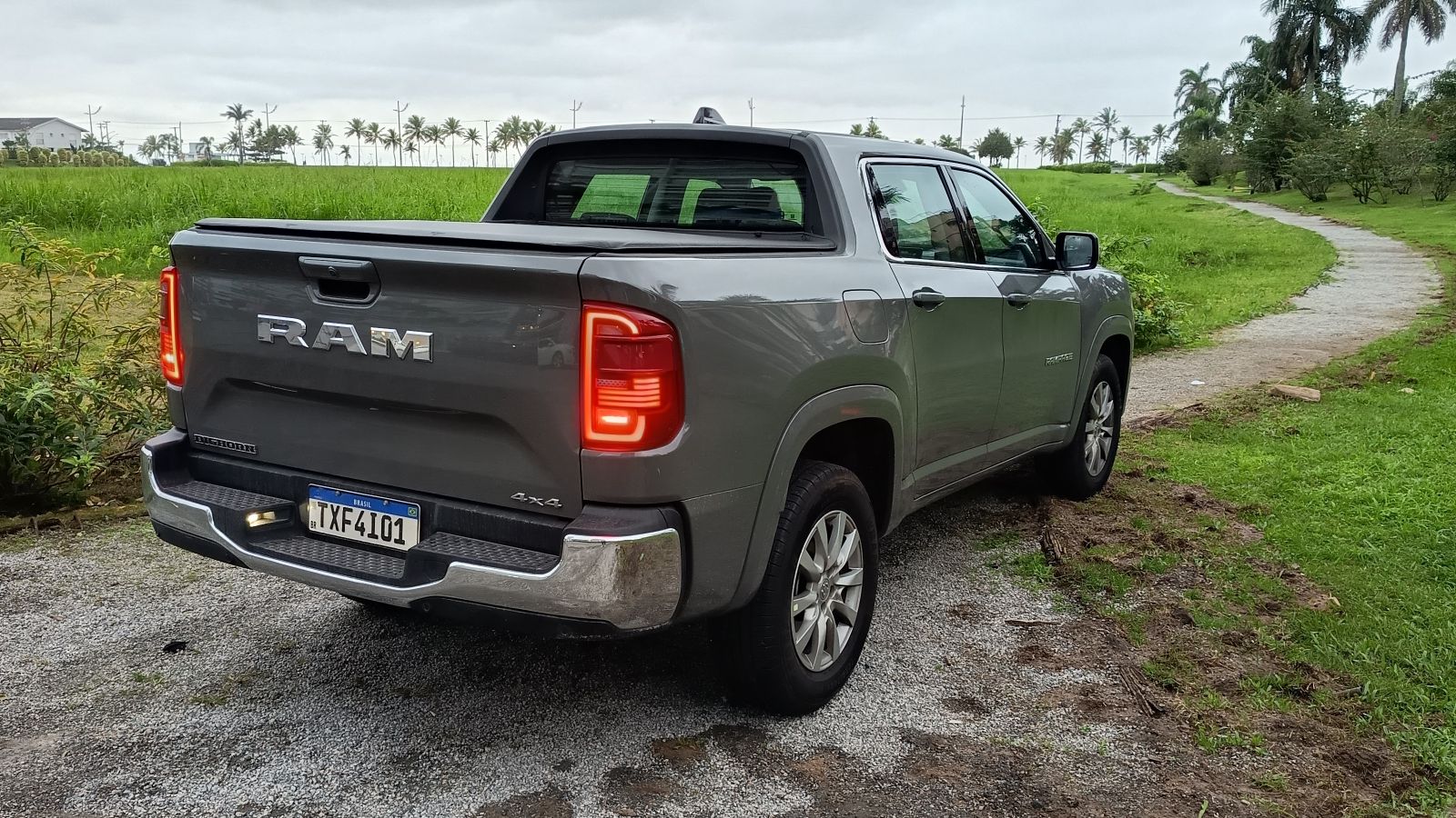 Imagem de uma caminhonete Ram 4x4 estacionada em uma área verde, com estrada de cascalho ao fundo.
