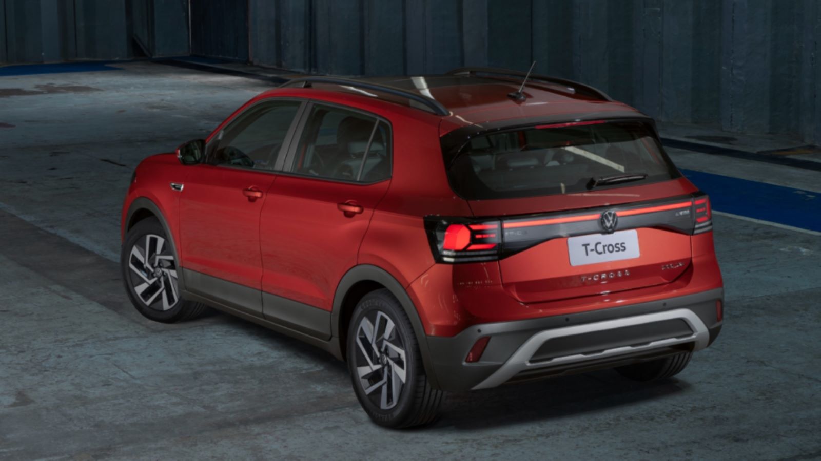 Um Volkswagen T-Cross vermelho estacionado em um espaço industrial com piso de concreto.