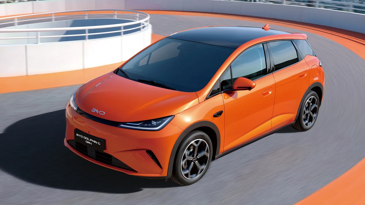Carro elétrico BYD Dolphin em movimento em uma pista circular, com pintura laranja e teto preto.