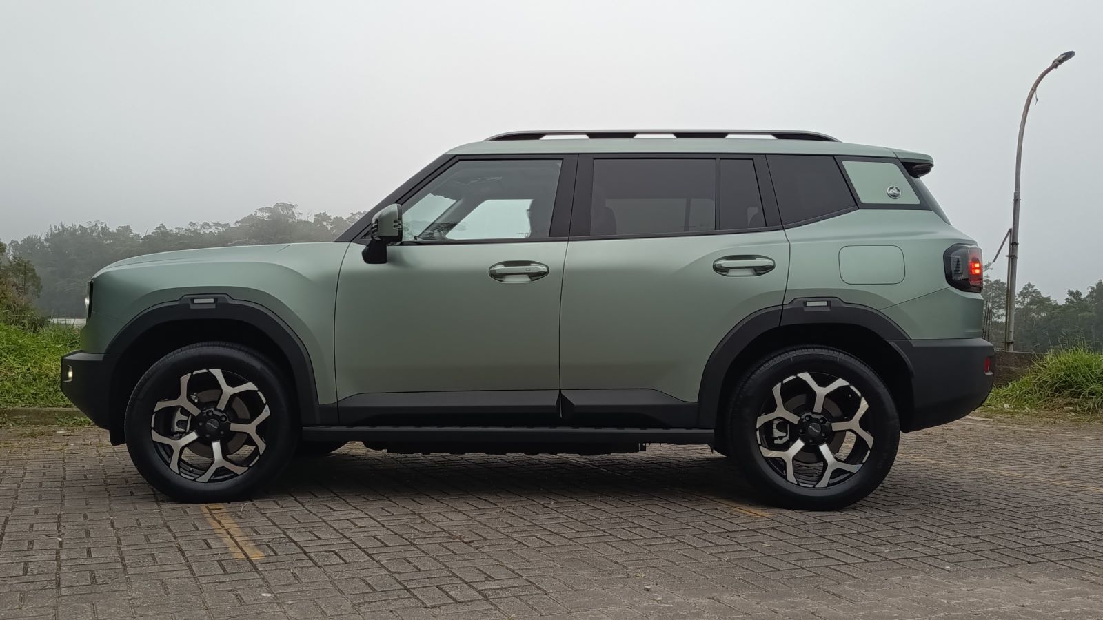 SUV verde claro com rodas de liga leve, estacionado em uma área aberta, com neblina ao fundo.