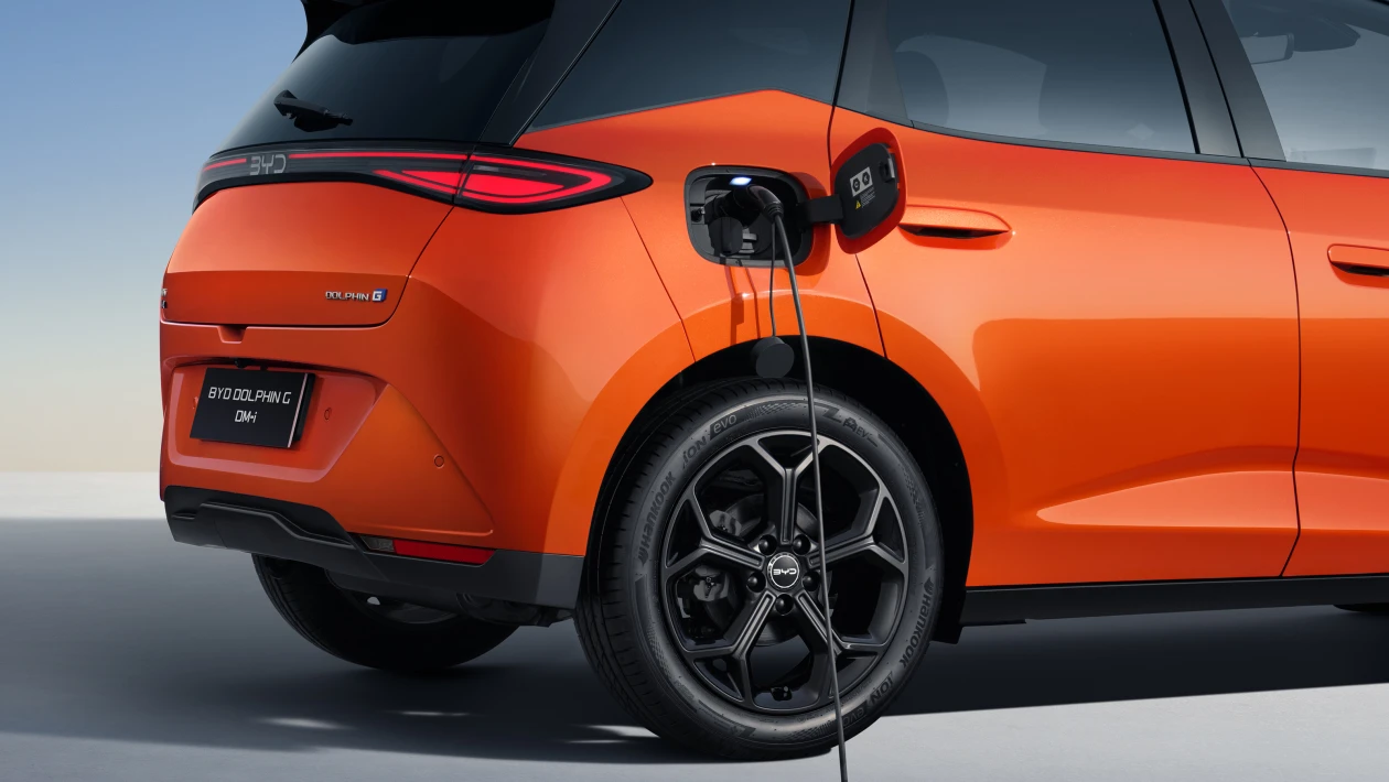 Imagem de um carro elétrico BYD Dolphin G na cor laranja, com um cabo de carregamento conectado ao lado traseiro.