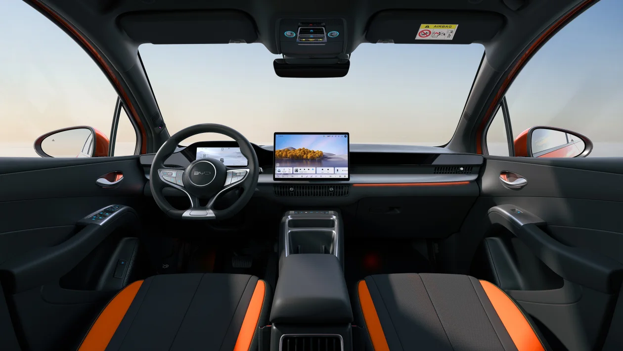 Painel interno de um carro moderno, destacando o volante, um grande display central e bancos com acabamento em preto e laranja.