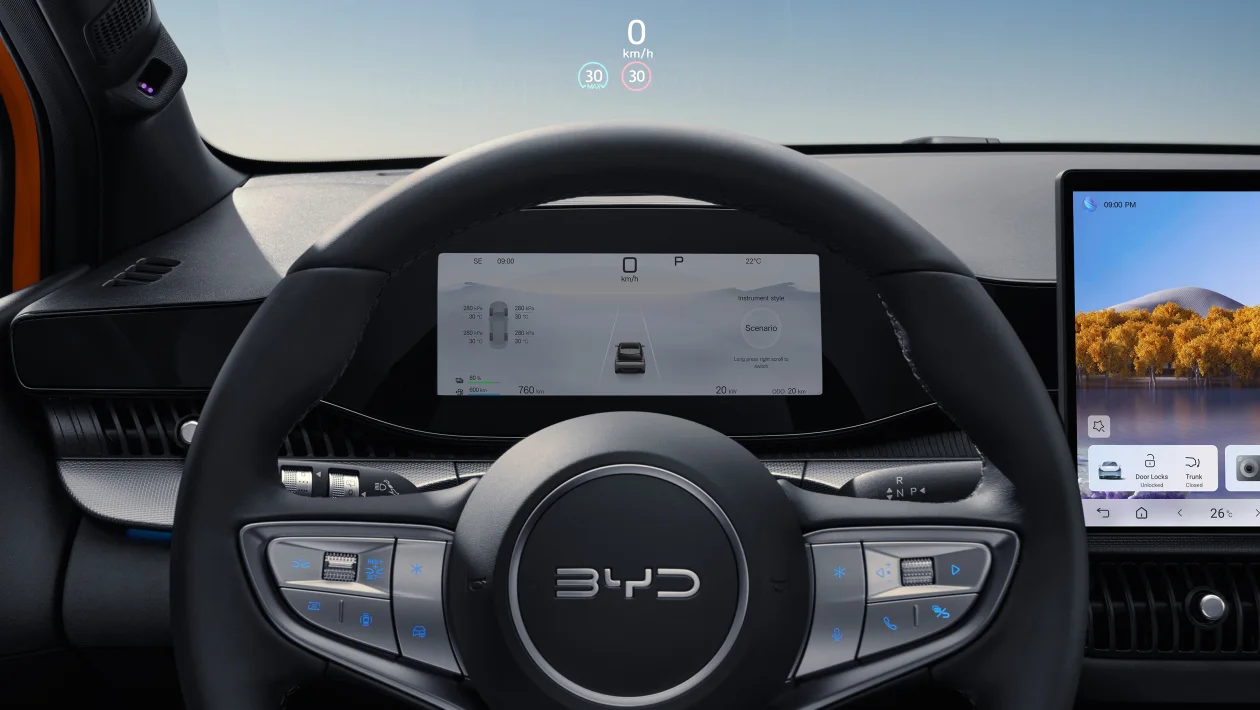 Interior moderno de um carro elétrico, mostrando o volante, painel digital e tela central com informações de velocidade e configurações.